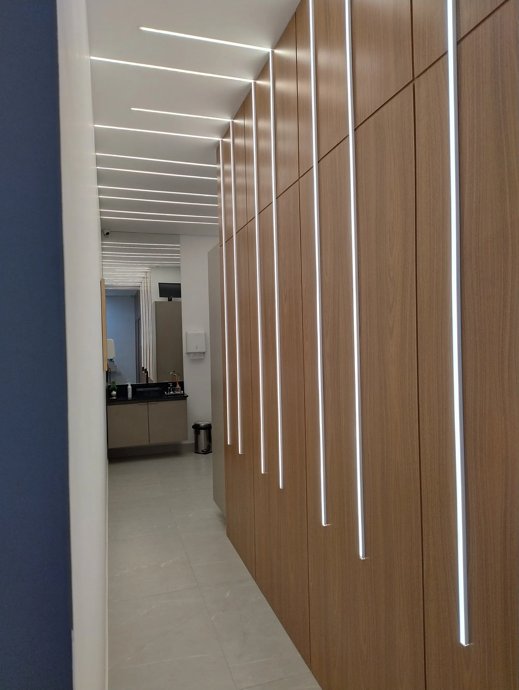 Corredor com painéis de madeira contínuos e frisos de iluminação LED vertical que se estendem pelo teto.