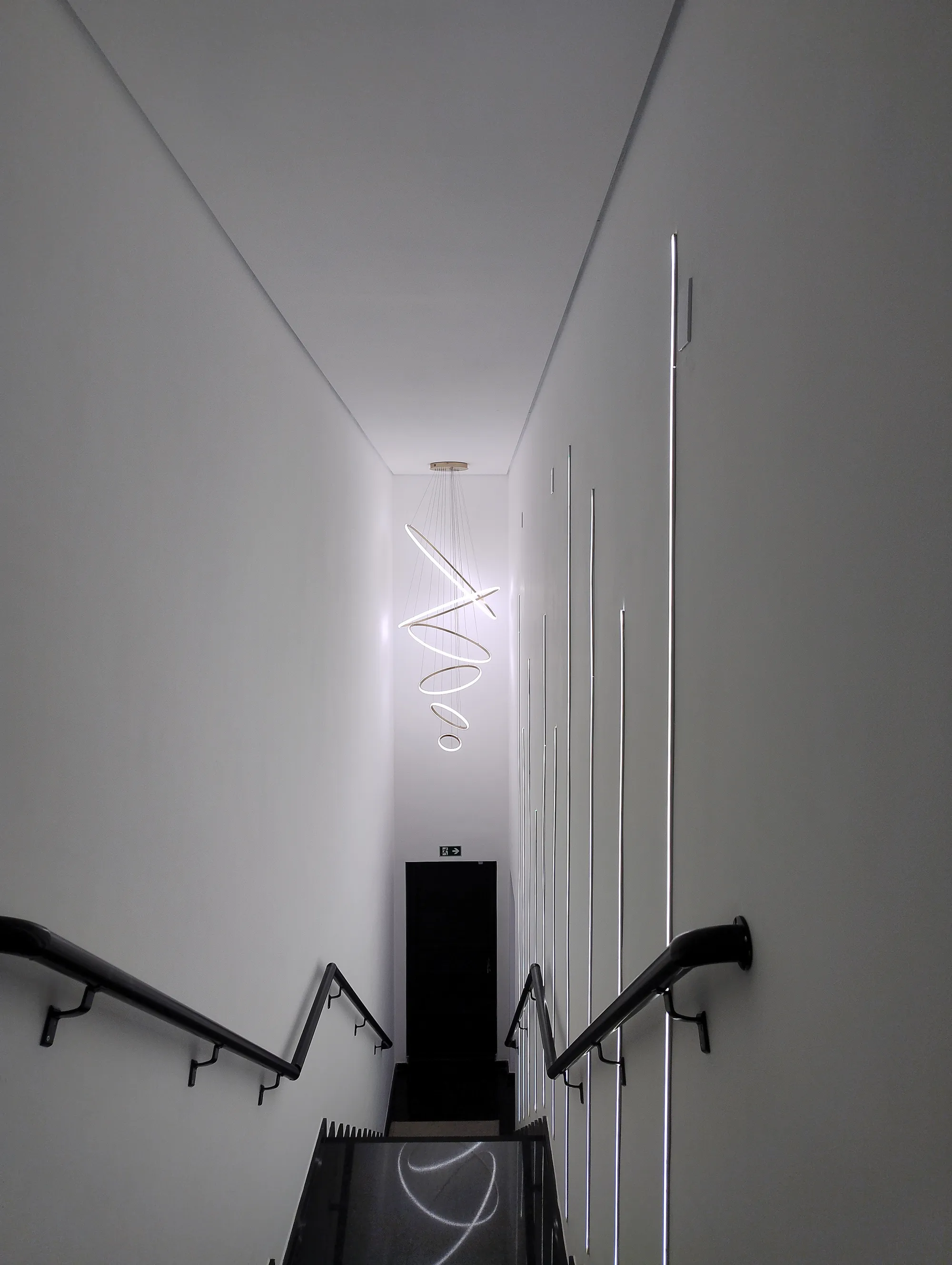 Vista superior da escada em granito preto, destacando um grande lustre pendente em espiral de LED.